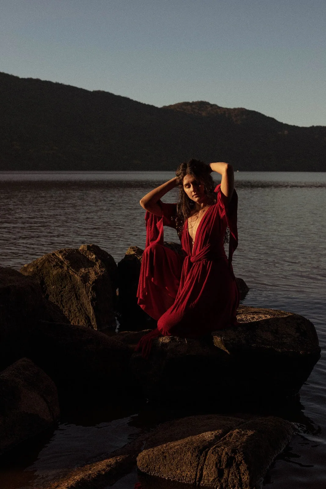 Kalina Cunha em vestido vermelho à beira de um lago ao entardecer