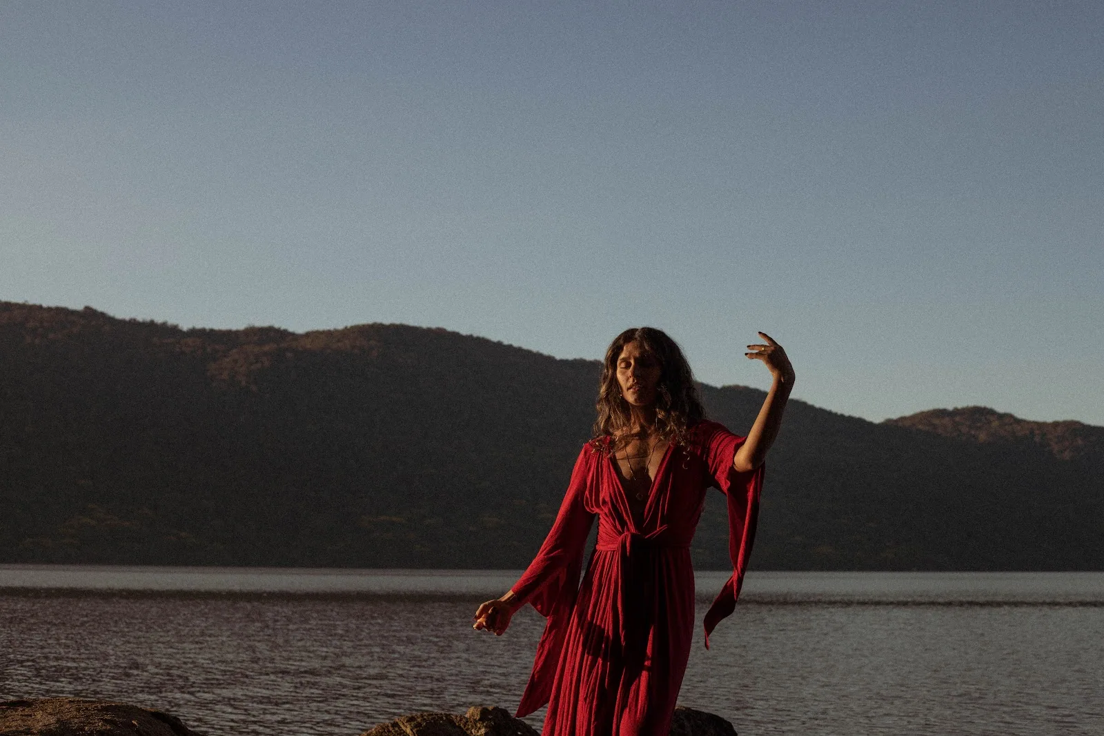 Mulher de vestido vermelho diante do lago e da montanha ao entardecer