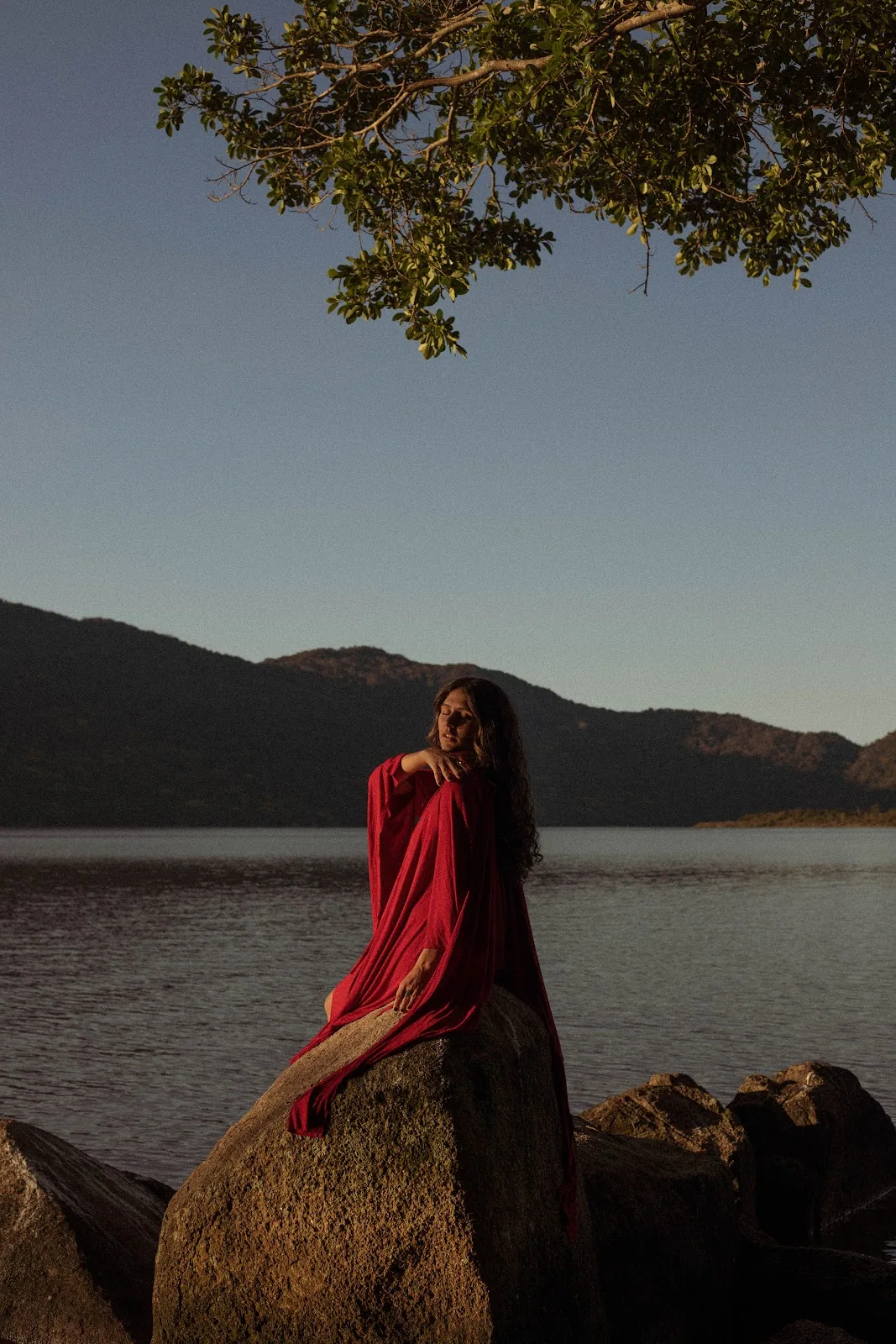 Kalina Cunha à beira do lago erguendo uma folha de palmeira ao entardecer